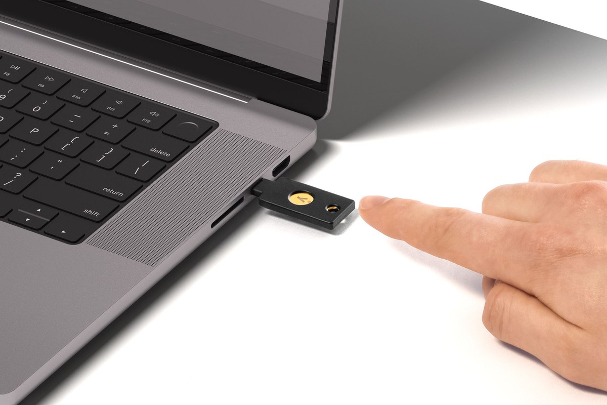 YubiKey 5C NFC plugged into a laptop, with a finger about to touch the gold contact